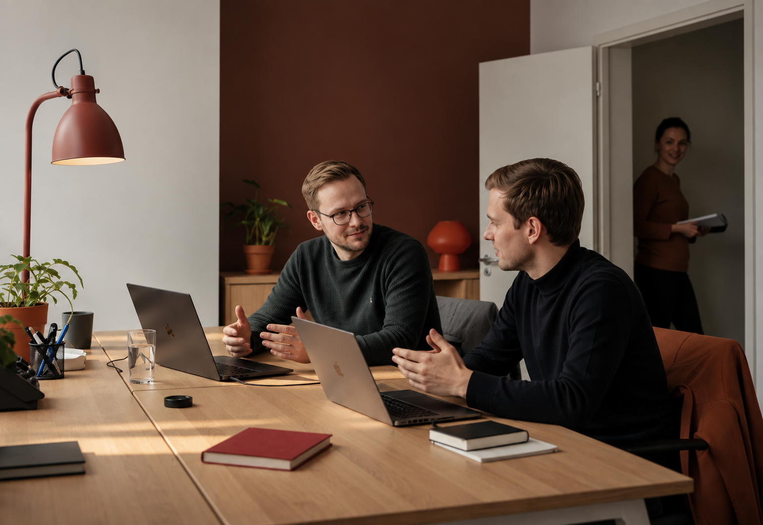 Two colleagues working at laptops in an office, a third walking in behind them